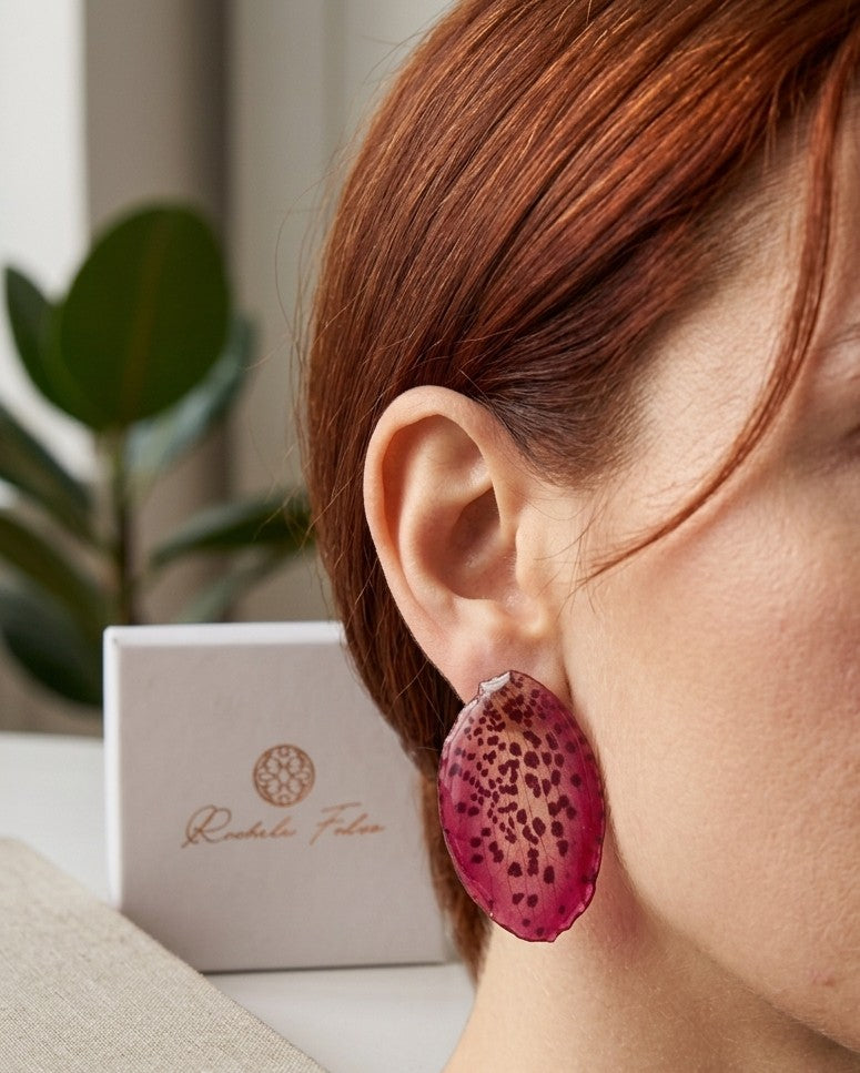 Orecchini a perno con chiusura a farfalla realizzati con petali veri di orchidea rosso amaranto dalla trama maculata, esposti sopra la loro scatola regalo bianca con logo Rachele Falvo.