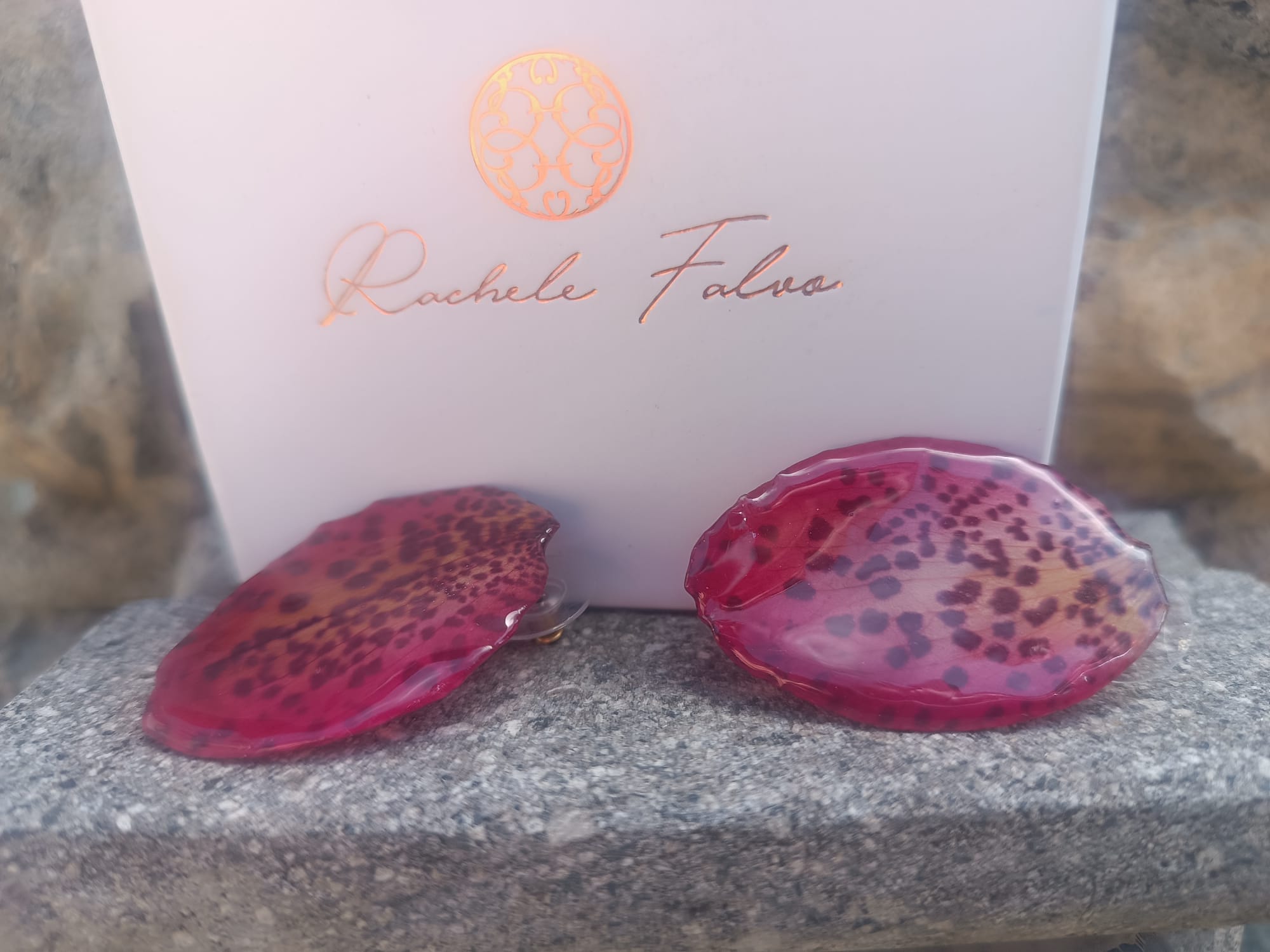 Orecchini a perno con chiusura a farfalla realizzati con petali veri di orchidea rosso amaranto dalla trama maculata, esposti sopra la loro scatola regalo bianca con logo Rachele Falvo.