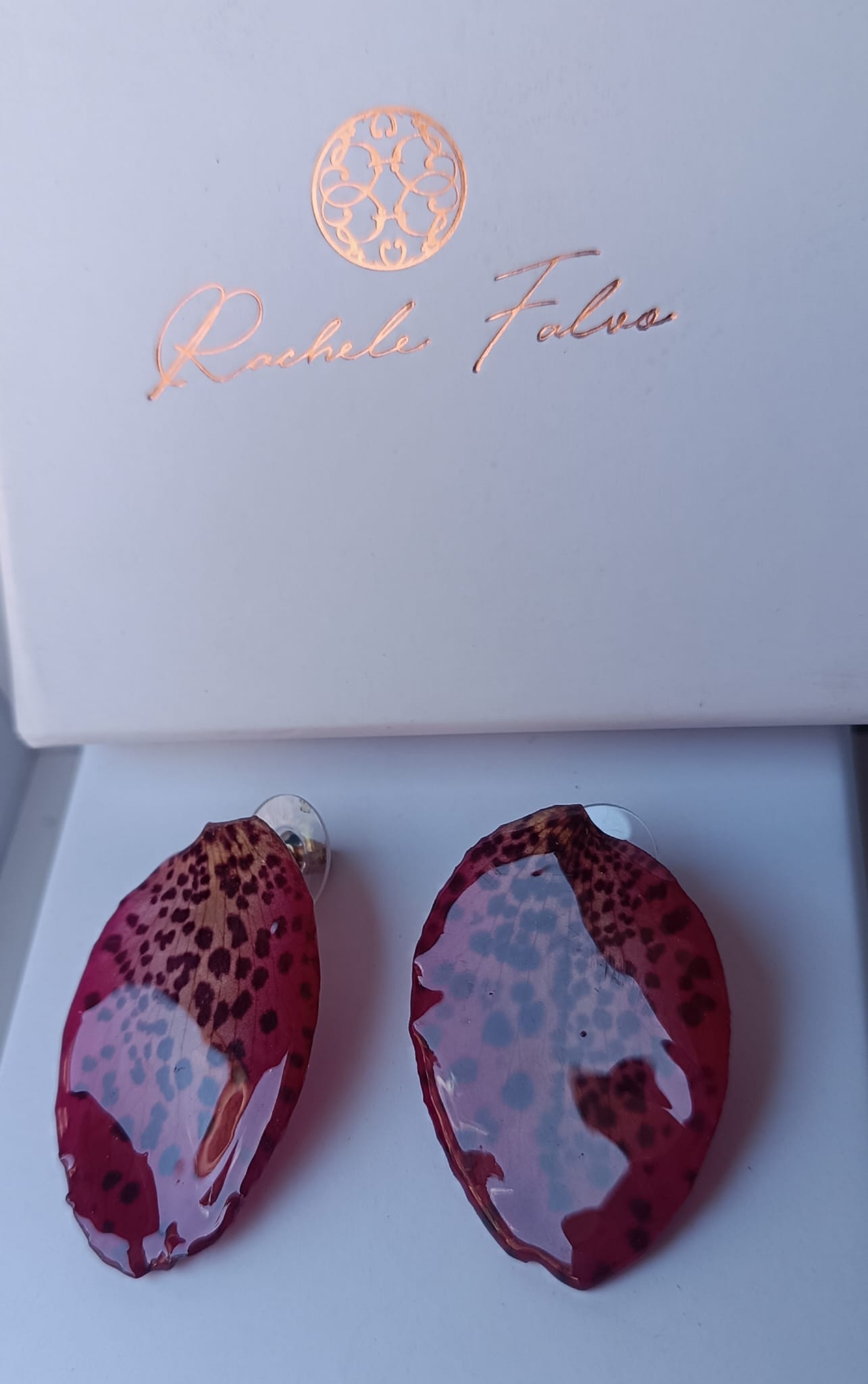 Orecchini a perno con chiusura a farfalla realizzati con petali veri di orchidea rosso amaranto dalla trama maculata, esposti sopra la loro scatola regalo bianca con logo Rachele Falvo.