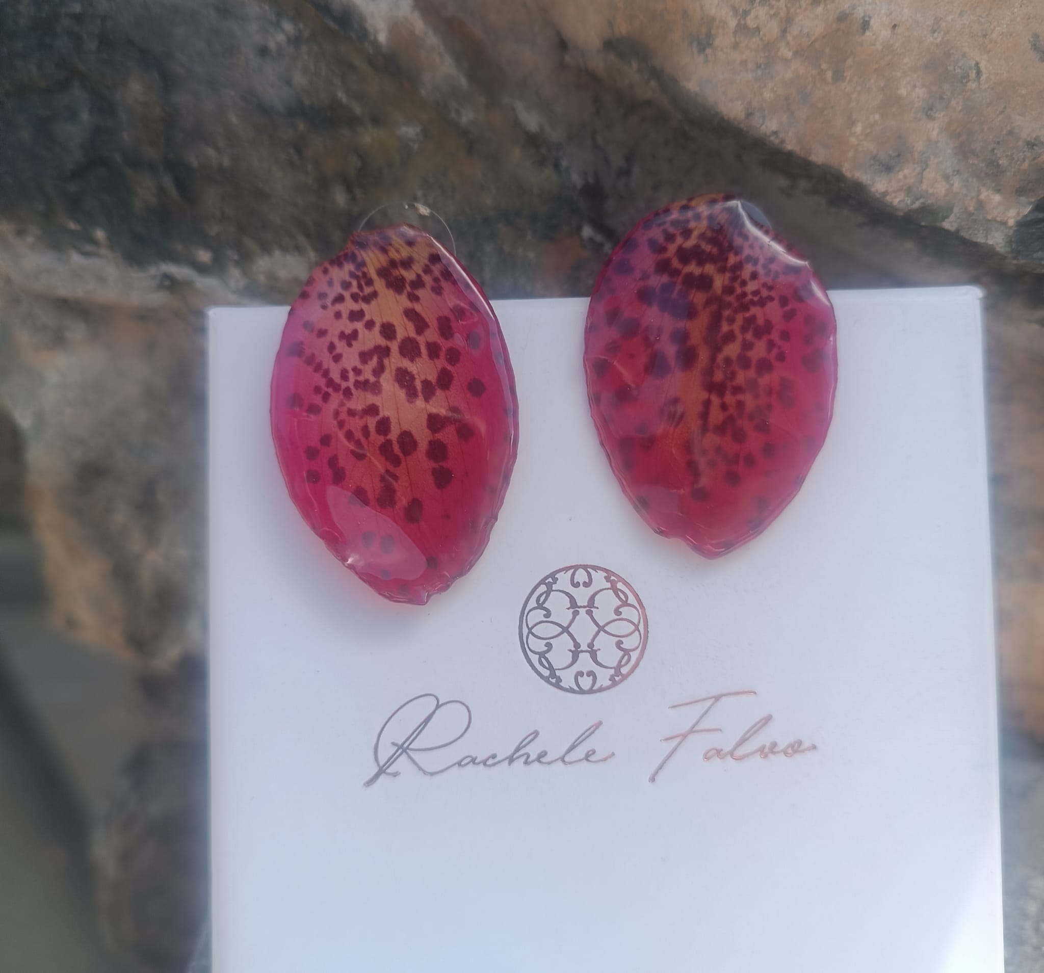Orecchini a perno con chiusura a farfalla realizzati con petali veri di orchidea rosso amaranto dalla trama maculata, esposti sopra la loro scatola regalo bianca con logo Rachele Falvo.