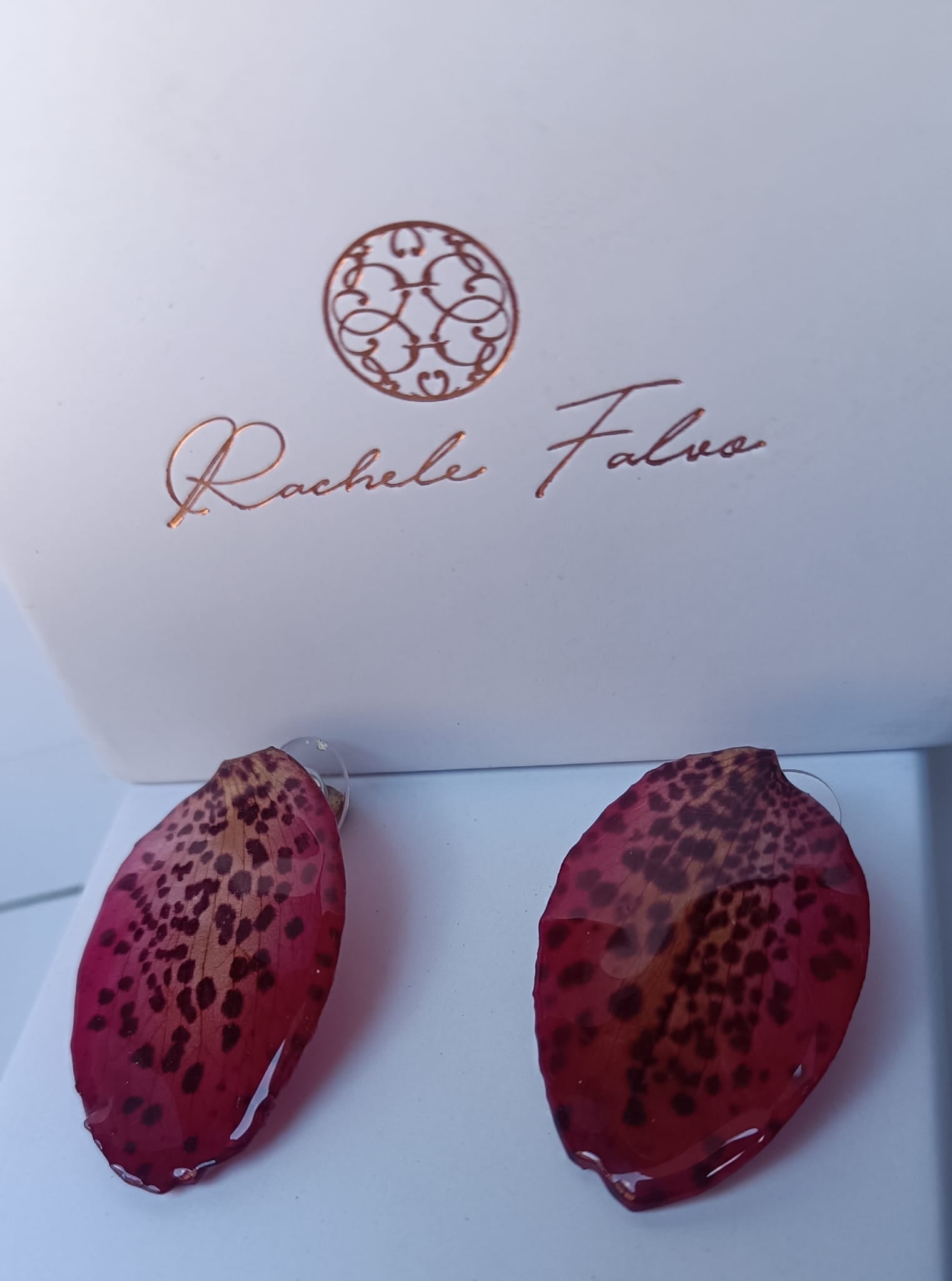 Orecchini a perno con chiusura a farfalla realizzati con petali veri di orchidea rosso amaranto dalla trama maculata, esposti sopra la loro scatola regalo bianca con logo Rachele Falvo.