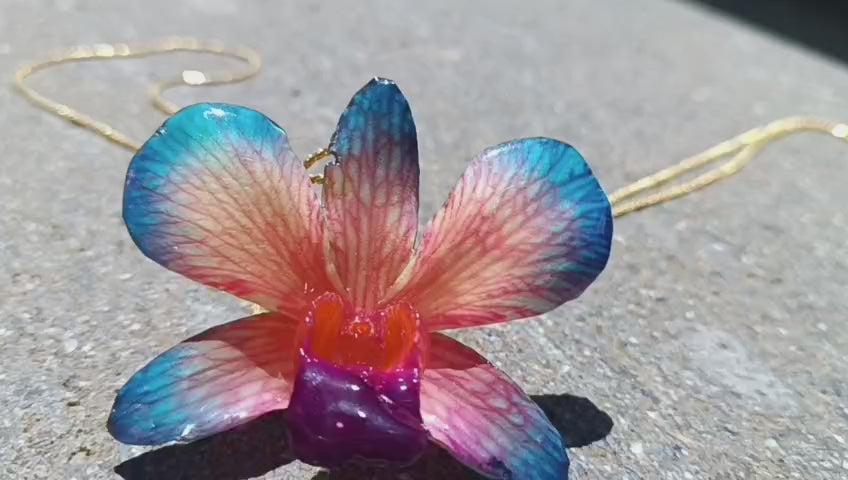 Collana con orchidea naturale azzurra e rossa inglobata in resina e saliscendi oro su bronzo regolabile